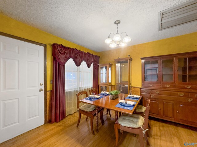 dining area featuring light wood-type flooring, a chandelier, and a textured ceiling