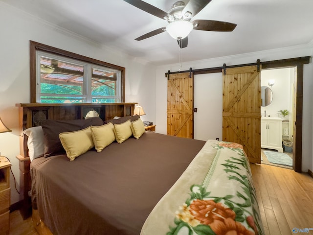 bedroom with a barn door, wood-type flooring, crown molding, ceiling fan, and ensuite bathroom