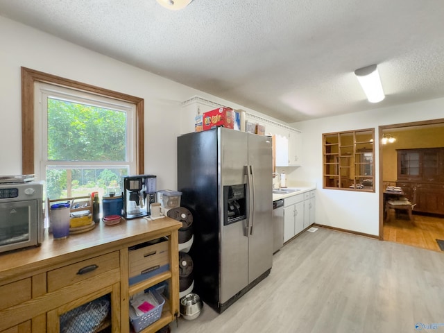 kitchen featuring stainless steel appliances, white cabinets, light hardwood / wood-style floors, and a textured ceiling