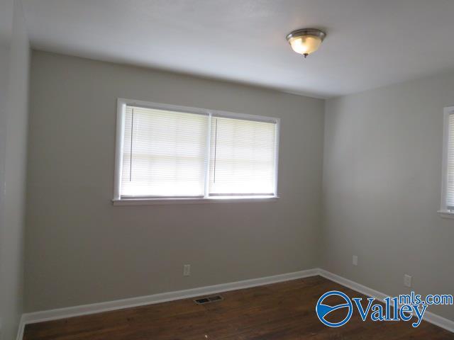 spare room with wood finished floors, visible vents, and baseboards