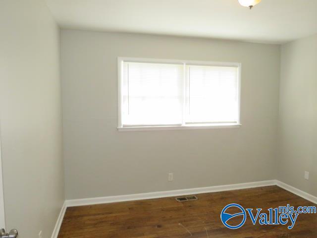 spare room with baseboards, visible vents, and wood finished floors