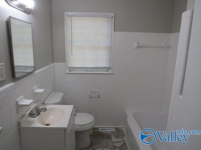 bathroom with toilet, vanity, visible vents, marble finish floor, and wainscoting