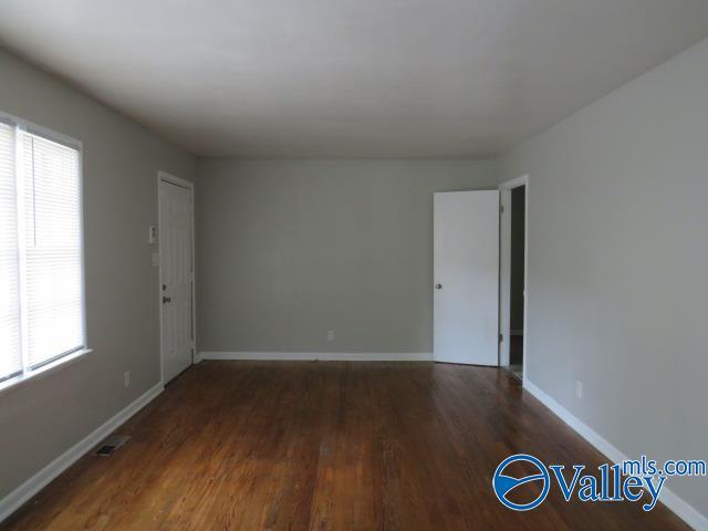 empty room with wood finished floors, visible vents, and baseboards