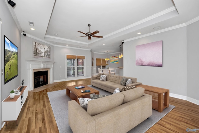 living room with ceiling fan, light hardwood / wood-style floors, ornamental molding, and a tray ceiling