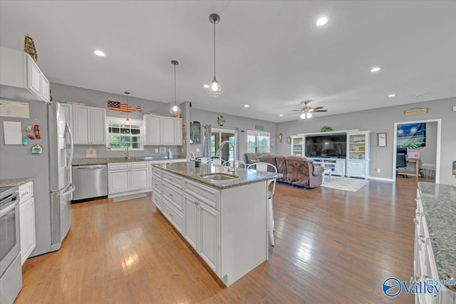 kitchen featuring light wood-style flooring, appliances with stainless steel finishes, open floor plan, white cabinets, and a sink