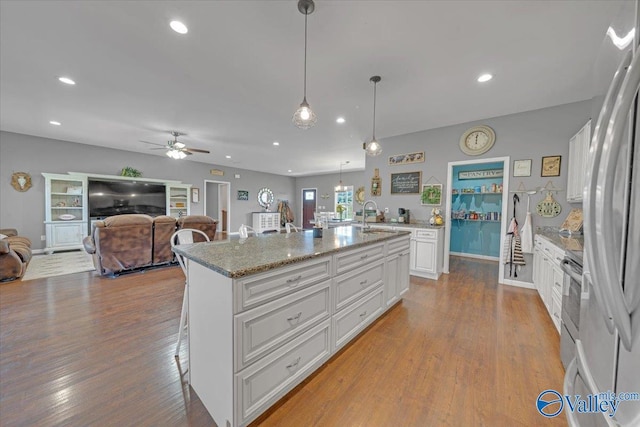 kitchen with a kitchen breakfast bar, an island with sink, wood finished floors, and white cabinets