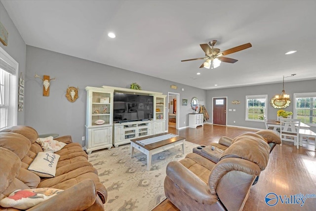 living room featuring ceiling fan with notable chandelier, baseboards, wood finished floors, and recessed lighting