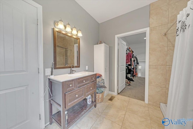 bathroom with a spacious closet, tiled shower, tile patterned flooring, and vanity