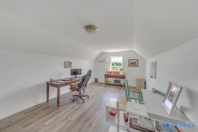 office area with baseboards, lofted ceiling, a textured ceiling, an AC wall unit, and light wood-type flooring