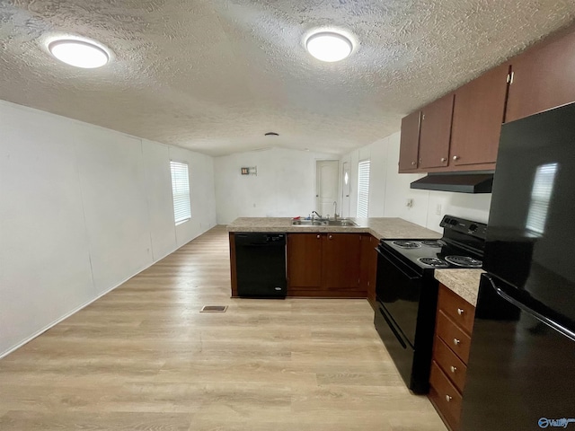 kitchen with light countertops, a peninsula, light wood-type flooring, under cabinet range hood, and black appliances
