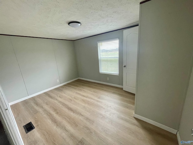 unfurnished bedroom featuring a textured ceiling, baseboards, visible vents, and light wood-style floors