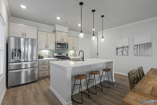 kitchen featuring appliances with stainless steel finishes, dark hardwood / wood-style floors, sink, hanging light fixtures, and a center island with sink