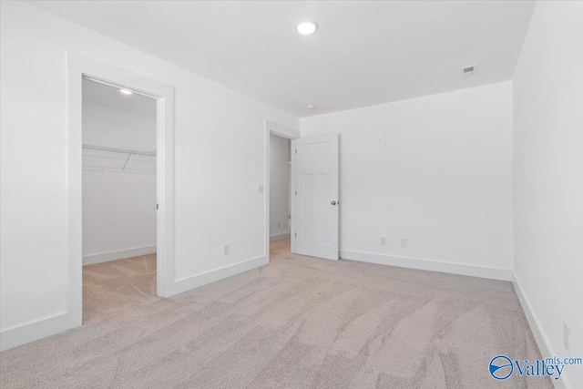 unfurnished bedroom with a walk in closet, a closet, and light colored carpet