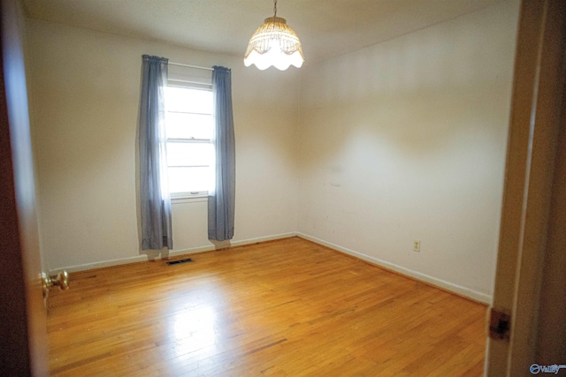 spare room featuring visible vents, baseboards, an inviting chandelier, and light wood-style flooring