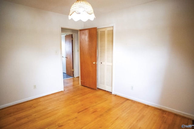 empty room with light wood-type flooring, baseboards, and an inviting chandelier