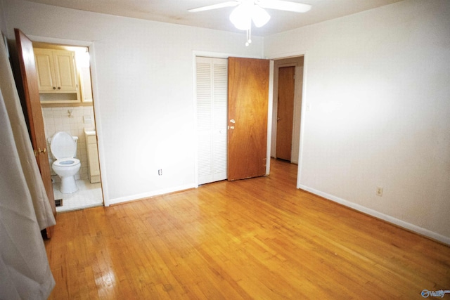 unfurnished bedroom featuring baseboards, light wood finished floors, ensuite bath, a closet, and tile walls