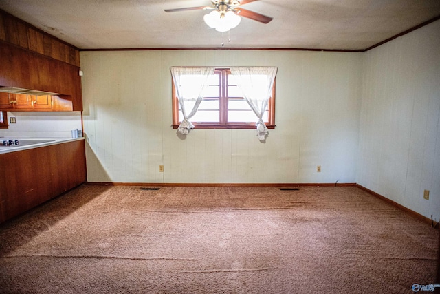 interior space with a ceiling fan, brown cabinetry, carpet, baseboards, and ornamental molding