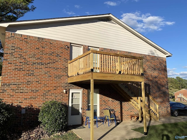 back of house featuring stairs, brick siding, a patio area, and a wooden deck