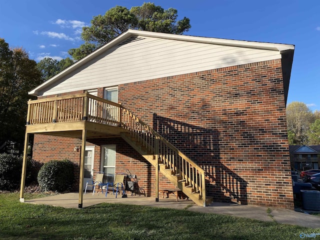 rear view of property featuring brick siding, a patio, a lawn, stairway, and a wooden deck