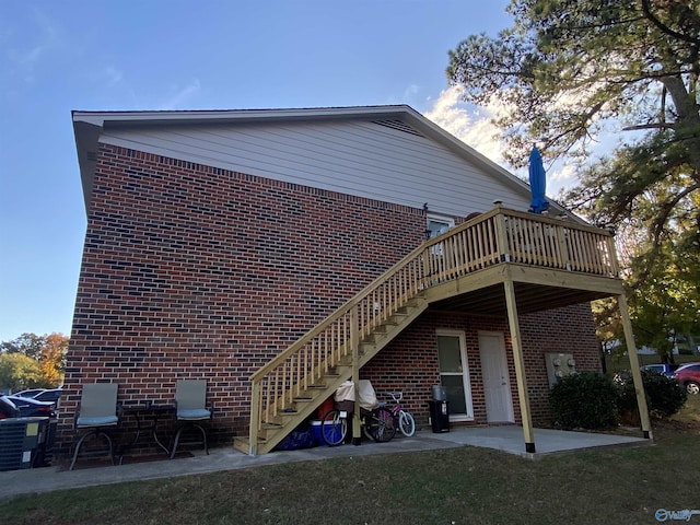 rear view of house with a patio area, a wooden deck, stairs, and brick siding