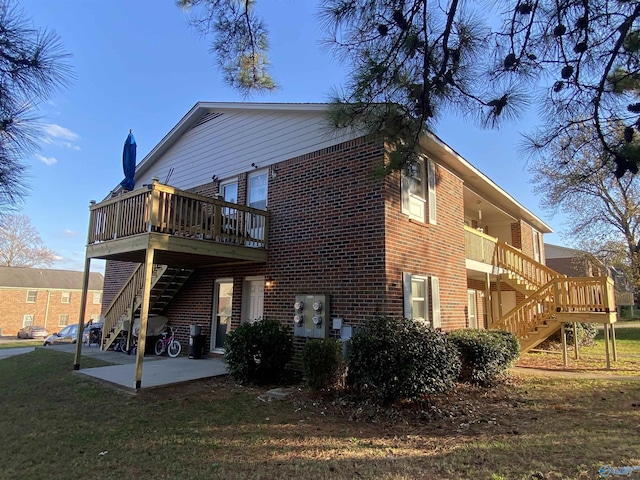 back of house featuring a lawn, a patio, stairs, a wooden deck, and brick siding