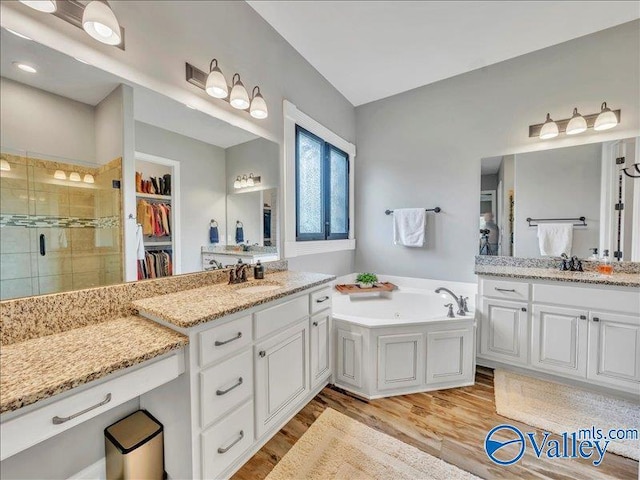 bathroom featuring wood finished floors, a garden tub, a stall shower, and two vanities