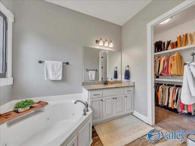 full bathroom with a spacious closet, a tub with jets, wood finished floors, and vanity