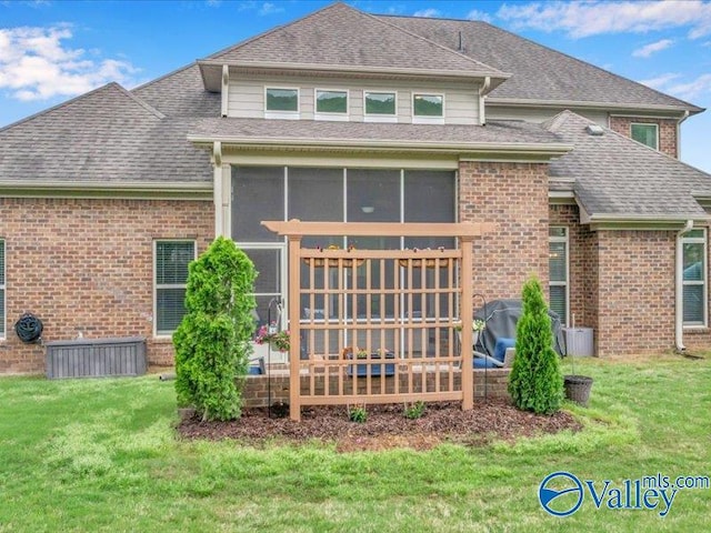 back of house with brick siding, a shingled roof, a yard, and a sunroom
