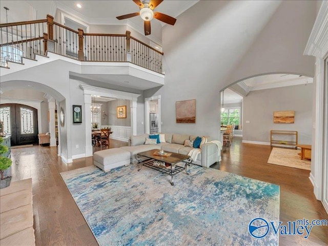 living room featuring a towering ceiling, arched walkways, wood finished floors, baseboards, and ceiling fan with notable chandelier