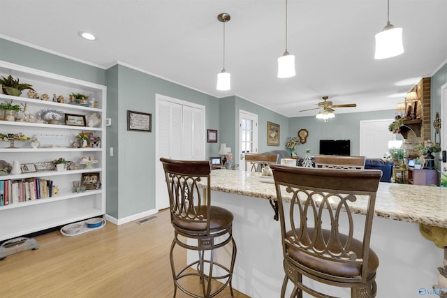 kitchen featuring light stone countertops, light hardwood / wood-style floors, a kitchen breakfast bar, hanging light fixtures, and ceiling fan