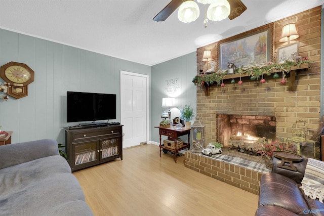 living room with ceiling fan, wood-type flooring, ornamental molding, and a fireplace