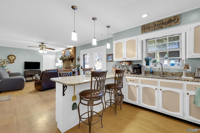 kitchen featuring white cabinetry, ceiling fan, hanging light fixtures, light stone countertops, and a breakfast bar