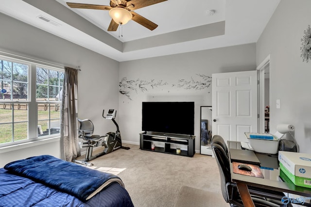 carpeted bedroom featuring a ceiling fan, a tray ceiling, baseboards, and visible vents