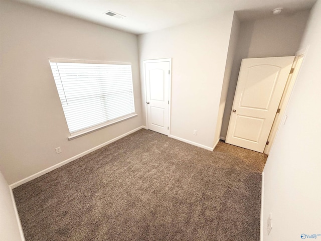 unfurnished bedroom with dark colored carpet, visible vents, and baseboards