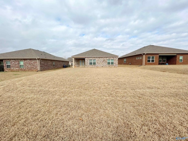 rear view of house featuring cooling unit, a lawn, and brick siding