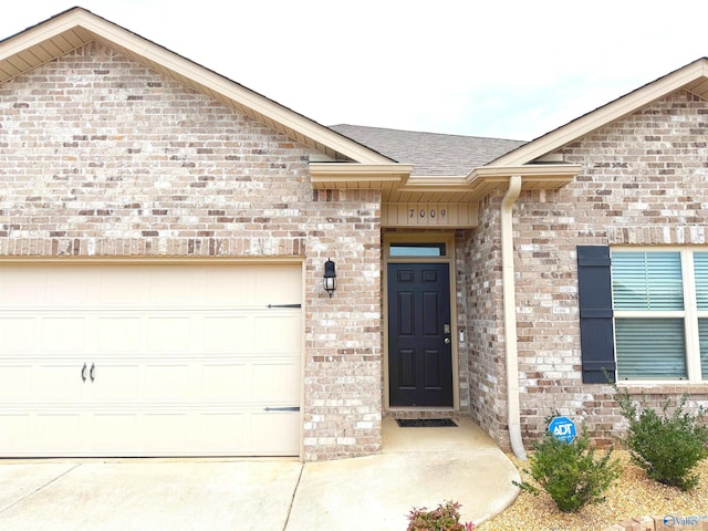 view of exterior entry with concrete driveway, a garage, brick siding, and roof with shingles