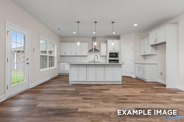 kitchen featuring wall chimney exhaust hood, white cabinets, decorative light fixtures, and a center island with sink