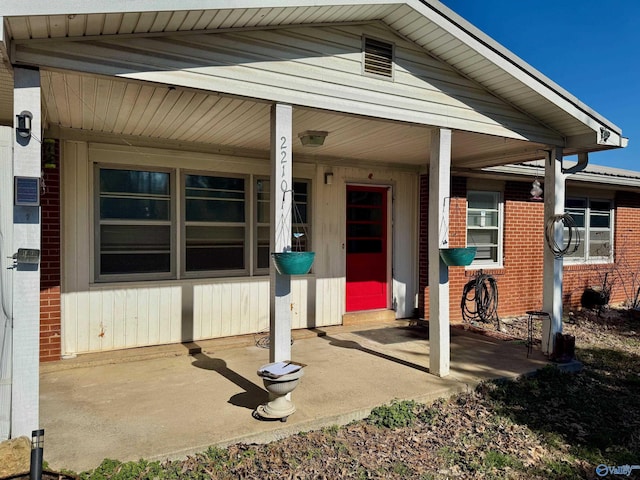 doorway to property with a porch and brick siding