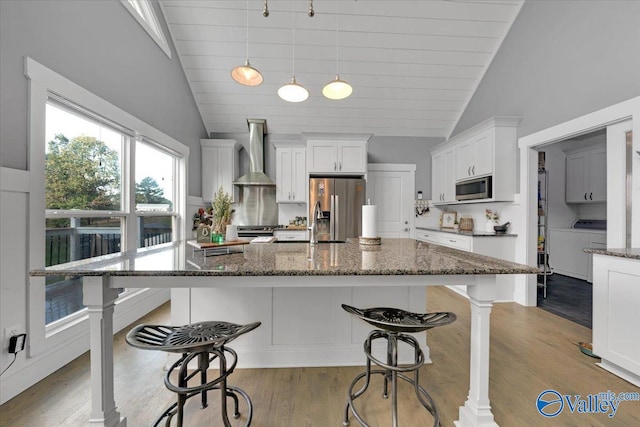 kitchen featuring wall chimney exhaust hood, light hardwood / wood-style floors, stainless steel appliances, and vaulted ceiling