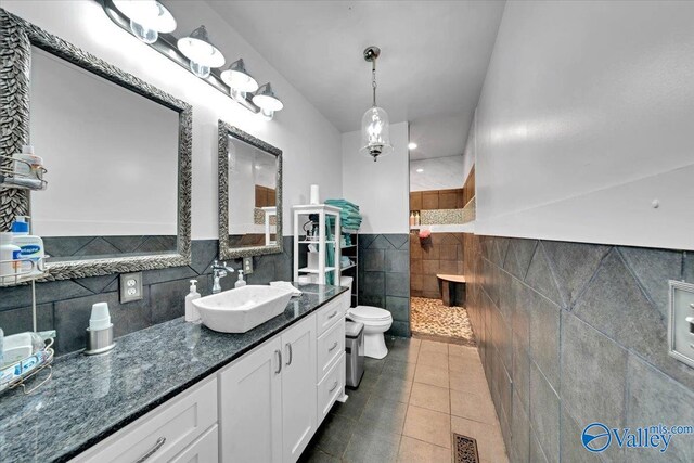 bathroom with toilet, vanity, tile patterned floors, and tile walls