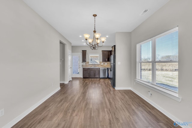 unfurnished dining area with dark wood-type flooring, a notable chandelier, sink, and a wealth of natural light