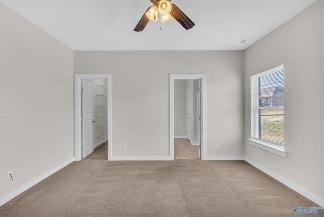 unfurnished bedroom featuring light carpet, a spacious closet, a closet, and ceiling fan