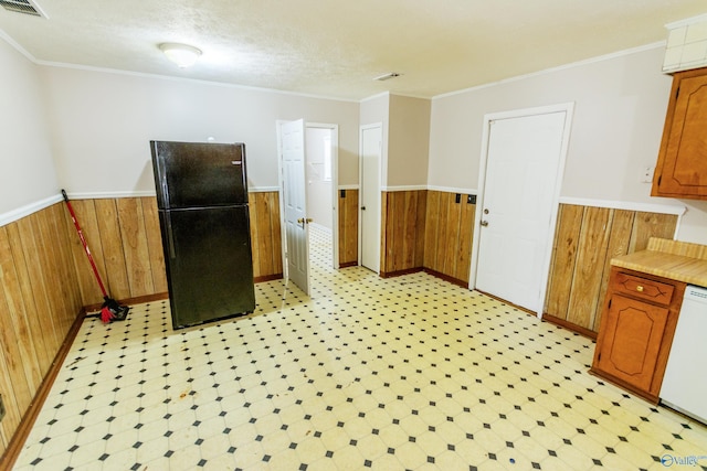 kitchen featuring crown molding, wooden walls, dishwasher, and black fridge