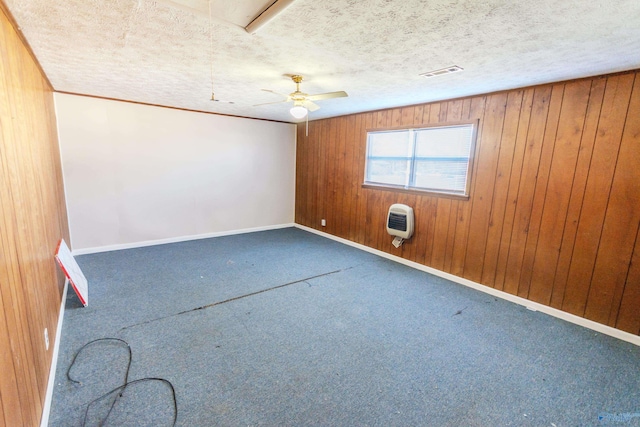 unfurnished room with heating unit, wood walls, carpet, ceiling fan, and a textured ceiling