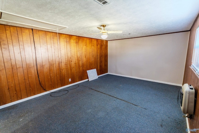 carpeted empty room featuring ceiling fan, heating unit, a textured ceiling, and wood walls