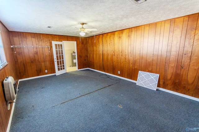 carpeted empty room featuring wood walls, ceiling fan, electric water heater, a textured ceiling, and french doors