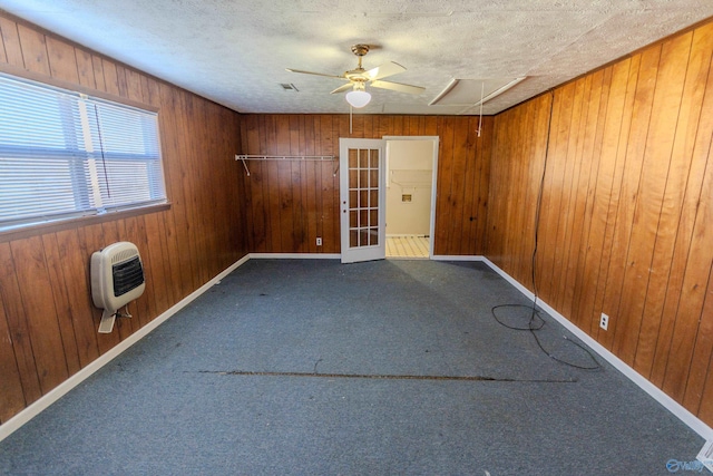 spare room with wooden walls, carpet flooring, heating unit, and a textured ceiling