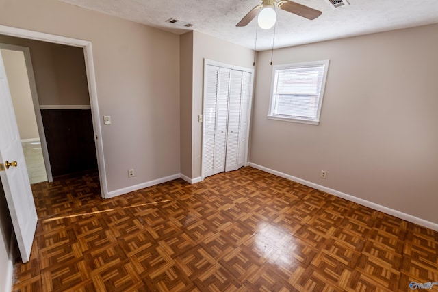 unfurnished bedroom with ceiling fan, a closet, dark parquet flooring, and a textured ceiling