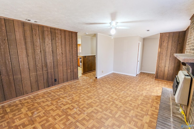 unfurnished living room with light parquet floors, wooden walls, heating unit, and a textured ceiling