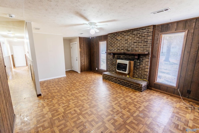 unfurnished living room with a fireplace, a textured ceiling, wooden walls, and a healthy amount of sunlight